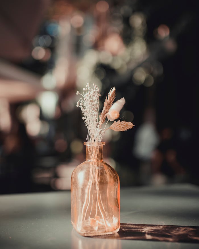 Elegant arrangement of delicate dried flowers in a glass vase with a blurred background for a moody atmosphere.