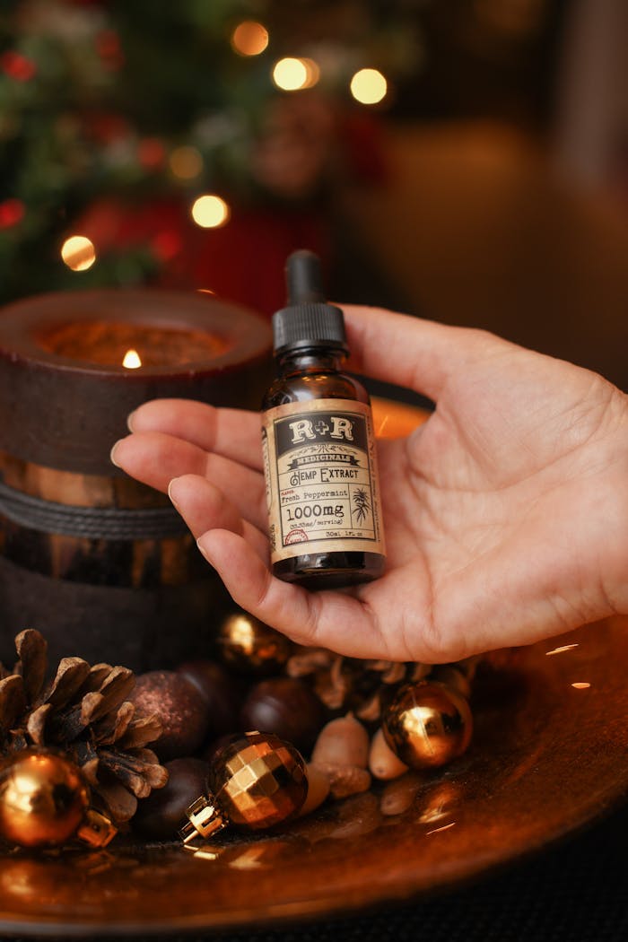 A close-up of a hand holding a hemp extract bottle surrounded by Christmas decor.