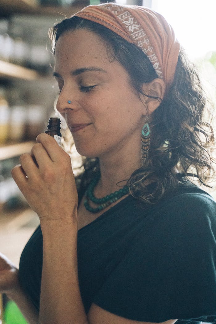A woman smelling essential oils indoors, enjoying a moment of relaxation and pleasant aroma.
