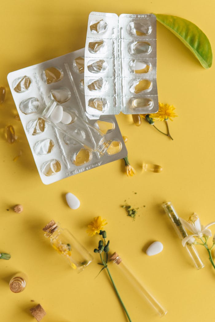 Flat lay of herbal medicine, pills, and empty blister packs on a yellow background.